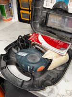Photo showing the Black & Decker Mouse sander, sanding sheets, and a tube inside the carrying case.