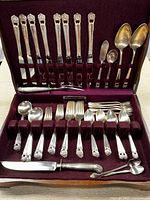 Full view of silverplated flatware set arranged inside an open fine wood box with burgundy velvet lining.