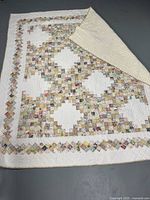 Photo of the vintage handmade quilt showing patchwork front and cream fabric backing folded at the corner.