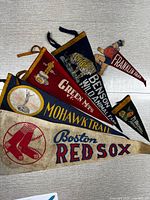 Six vintage red and blue felt pennants laid out showing Boston Red Sox and New England regional themes including sports and nature designs.