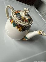 Side view of vintage ceramic tea pot with embossed and painted fruit design showing handle, spout, and lid details.