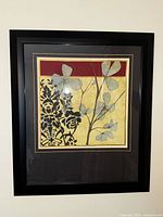 Framed wall art of abstract flowers with metallic silver leaves, black floral patterns, and a gold background bordered by red.