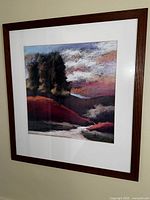 Framed abstract landscape wall art with hills and trees, wooden frame and glass front, displaying multi-colored sky and terrain.