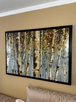 Framed canvas wall art showing birch trees in an abstract style, mounted on a beige wall above a pillow.