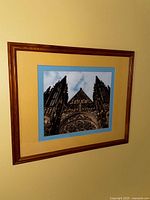 Framed wall art photograph of a church facade showing gothic architecture, tall spires, and detailed stone carvings. The frame is wood with glass and colored matting.