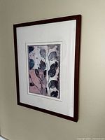 Photo of framed wall art printed with pressed leaves in muted colors, showing overall piece hung on wall.