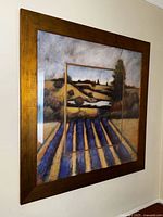 Framed wall art depicting a lavender field landscape with a wooden frame and glass cover, hanging on a wall.