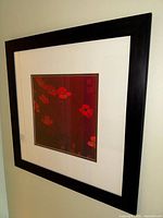 Photo of framed wall art depicting red poppies on dark red background, wooden frame with glass cover.