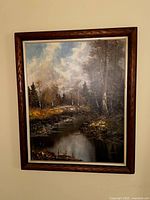 Framed canvas painting depicting a river flowing through woods with trees and a cloudy sky, measuring 28x2x34 inches.