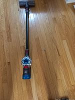 Dyson cordless stick vacuum cleaner placed on wooden floor showing the main body, cyclone assembly, dustbin and motorized brush head attachment.