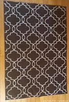 Image showing the full rectangular rug with a brown background and white geometric trellis pattern on a wooden floor.