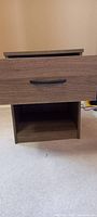 Front view of closed drawer nightstand showing wood grain finish and black metal drawer handle