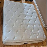 Top view of king mattress showing quilted tufted pattern and side tag on hardwood floor.