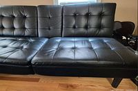 Black genuine leather foldable living room chair, tufted cushions visible, shown unfolded as a bed in living room setting.