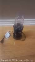Front view of Magic Bullet blender with clear blending cup attached, power cord and plug visible.