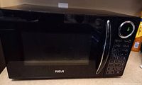 Front view of black RCA microwave with digital display turned on showing 0 seconds and control keypad to the right of the door.