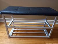 Side view of white metal frame shoe rack with two shelves and black cushioned seat showing metal bars and frame details.