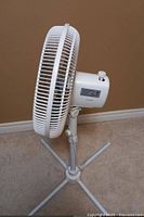 Side angled view of the white standing fan showing the motor housing, oscillation knob, and base.