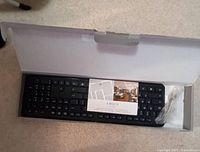 Photo showing the black wireless keyboard in open box with user manual and USB receiver.