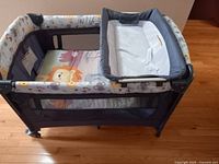 Side angled view showing entire bassinet, fabric liner with animal prints, mesh side panels, attached changing station, and wheels.