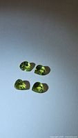 Four pear cut apple green peridot gemstones displayed on white background with clear light reflection showing facets