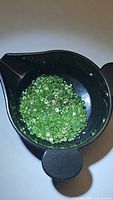 Close-up photo of a black container holding numerous small, light green, diamond cut tsavorite garnet stones