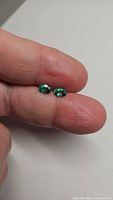 Close up image of two oval cut Colombian emerald gemstones held between fingers showing color and luster