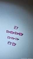 Photo of nine natural cotton candy pink sapphires in princess cut, arranged on surface with light and shadow.