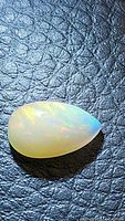 Pear-shaped fire opal on textured black background showing vibrant colors and translucent body.