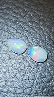 Pair of polished Ethiopian opals placed on black textured background showing vibrant rainbow flashes of color.