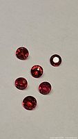Six round faceted rubies displayed on a white background showing their color and facets under natural light.