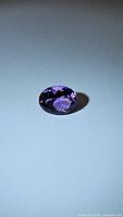 Photo of single oval cut natural untreated purple amethyst gemstone on plain background showing facets and rich purple color.