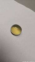 Natural oval lemon citrine cabochon gemstone on plain surface, showing its translucent lemon-yellow color and rounded polished dome shape.