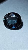 Close-up photo of the natural oval cut blue sapphire showing facets and deep blue color