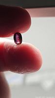 Close-up of the sapphire held between fingers showing deep purple pink color under diffused light.