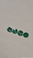 Four loose round cut green emerald stones placed in a line on a white surface viewed under natural light.