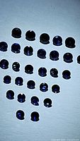 Image showing natural deep blue sapphires, round cut, laid out in 5 rows under bright light, total approximately 30 stones