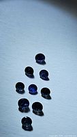 Ten natural blue sapphires, diamond cut, arranged on a white background showing various angles and light reflections.