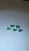 Five loose natural round cut emerald gemstones placed on white surface with illumination casting shadows.