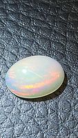 Close-up photo of a luminous oval cabochon natural Ethiopian opal showing vibrant rolling play of color on a dark textured background.