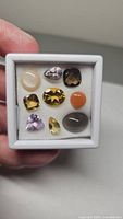 Photo showing a 9-piece mixed parcel of natural gemstones set in white foam box, including citrine, amethyst, moonstone, and smoky quartz with varying cuts and colors.