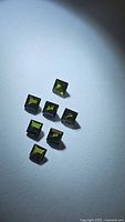 Seven princess cut green tourmaline gemstones arranged on a white surface, showing shape, color, and size.