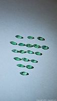 Multiple marquis cut natural emeralds arranged on a plain surface, showing their size, shape, cut, and color.