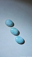 Three natural larimar oval cabochon gemstones arranged on a plain surface showing their color and marbling patterns.
