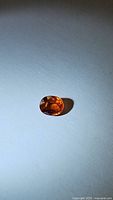 Oval cut Mandarin orange Spessartite garnet gemstone photographed against white background showing color and facets.