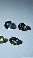 Close-up photo showing four faceted natural multicolored sapphires with green, blue, and yellow tones, arranged on a plain surface.