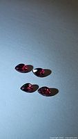 Four natural pear cut noble red spinel gemstones arranged on a white surface showing clarity and color.