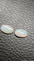 Two oval crystal Ethiopian opals on black textured background, showing subtle internal rainbow colors.