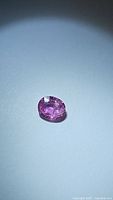 Oval cut natural pink sapphire gemstone on a neutral background, showing its color and clarity.