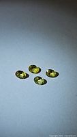 Four small oval-shaped natural sapphires in chartreuse yellow under bright light, showing clarity and color.